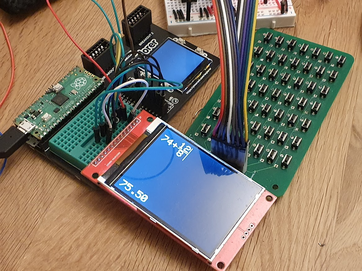 A Pimoroni Pico Explorer, with a board containing many tactile buttons, and the 2.8" display, connected to its breadboard. The display is showing a mathematical expression in crude font.