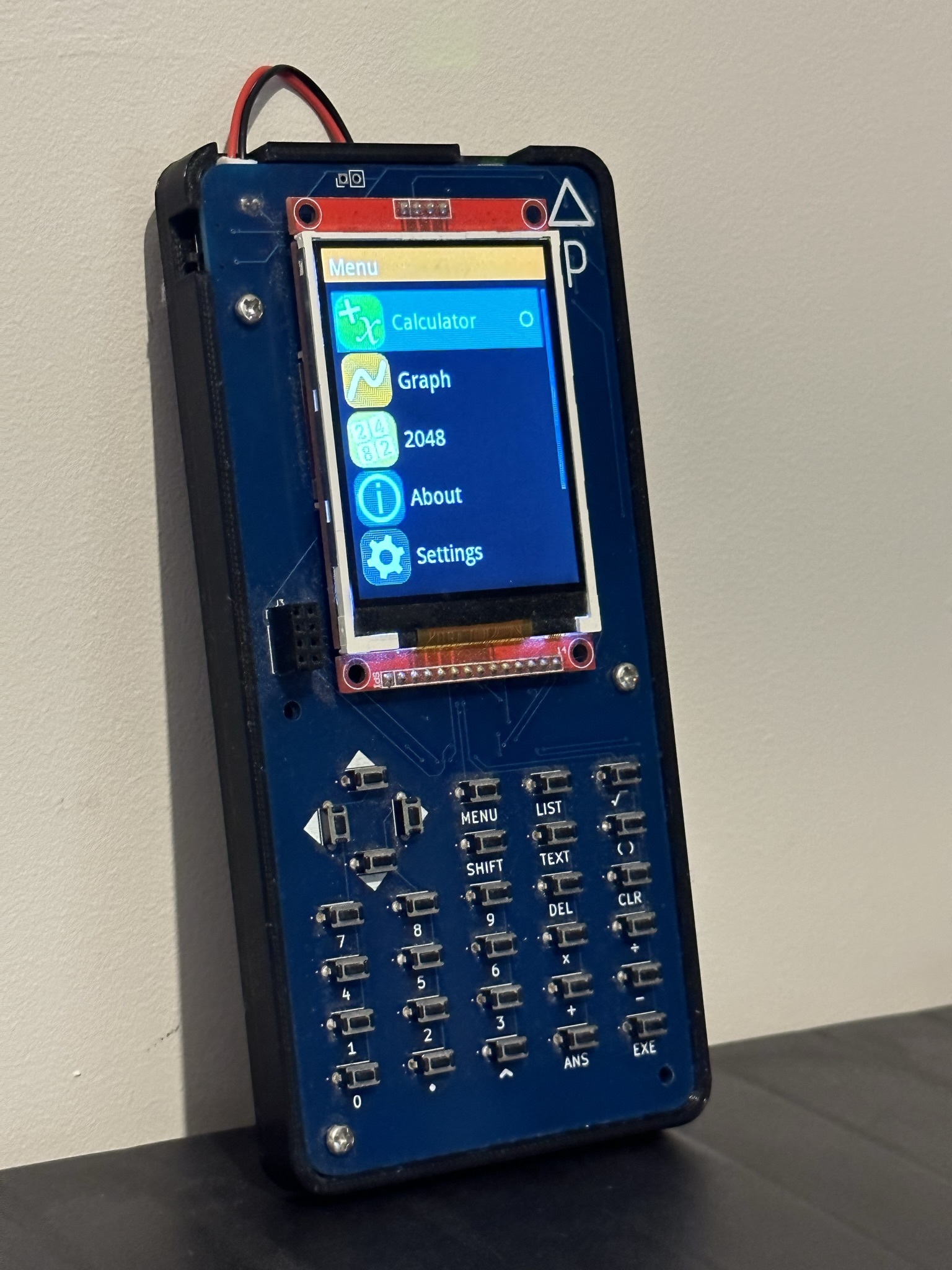The Delta Pico. Built on a blue PCB inside a black 3D-printed case, there is a 2.8" TFT display showing a main menu, below which lies a keypad of tactile buttons.